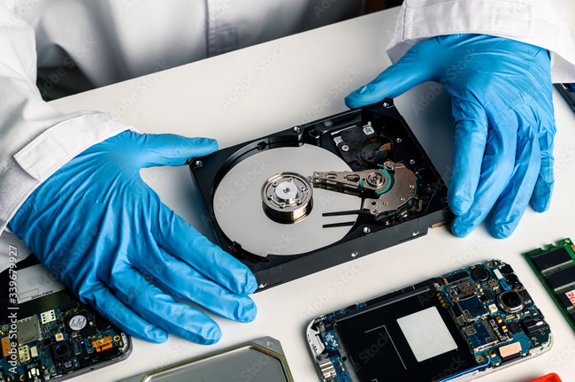 A person with blue latex gloves on has disassembled a comptuer hard drive and is performing "surgery" on it to recover data.