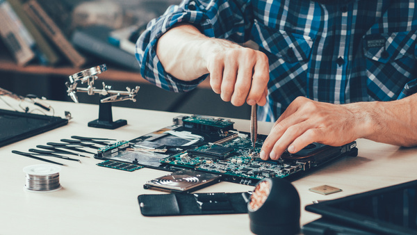 A man repairing a laptop with a screwdriver and other various tools